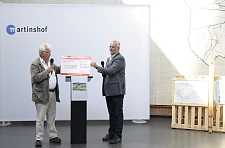 Auf der Bühne stehen zwei Personen. Der Check wird übergeben.