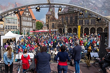 Auf einer Bühne wird während des Mitsingfestes gesungen. Vor der Bühne stehen Zuschauer.