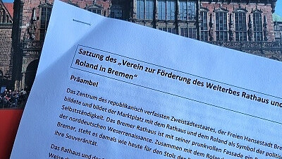 Die Satzung vom Verein zur Förderung des Welterbes Rathaus und Roland wird vor dem Bremer Rathaus hochgehalten.
